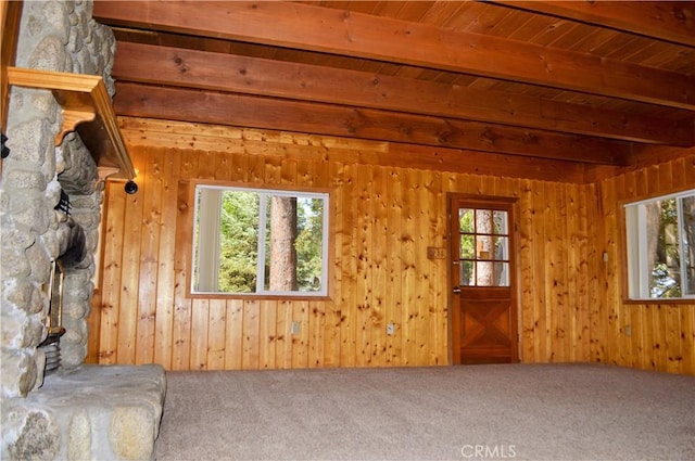 unfurnished living room featuring carpet flooring, wood walls, wooden ceiling, and beam ceiling