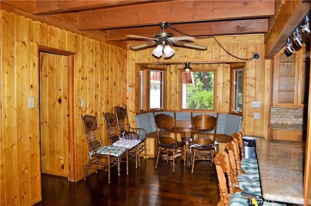 dining space featuring beam ceiling, dark hardwood / wood-style flooring, ceiling fan, and wood walls