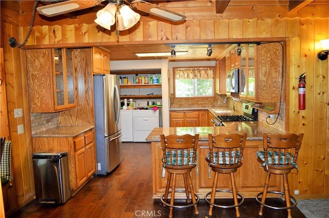 kitchen featuring wood walls, washing machine and dryer, kitchen peninsula, and appliances with stainless steel finishes