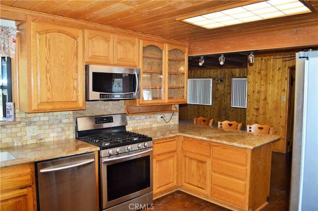 kitchen with stainless steel appliances, light stone counters, backsplash, kitchen peninsula, and wooden walls