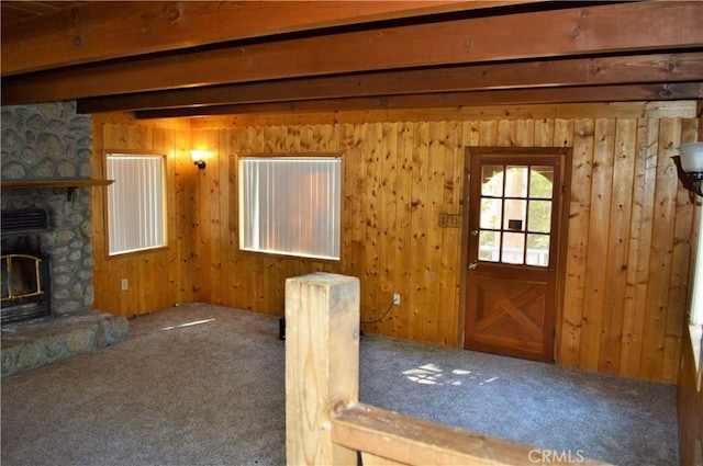 entryway featuring carpet, beam ceiling, a fireplace, and wooden walls