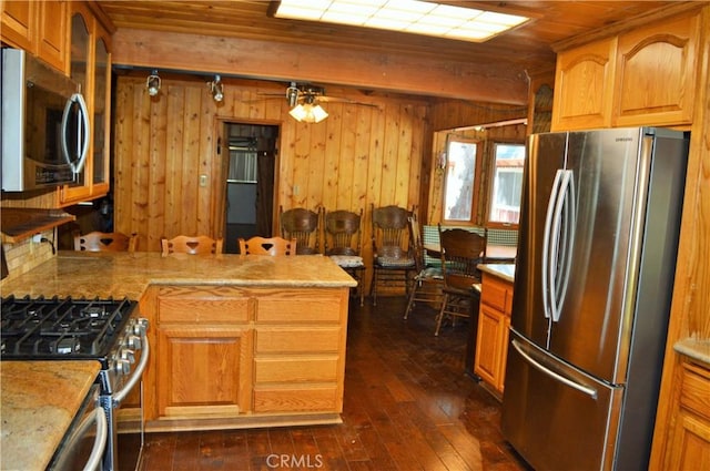 kitchen with kitchen peninsula, wood walls, dark hardwood / wood-style flooring, and appliances with stainless steel finishes