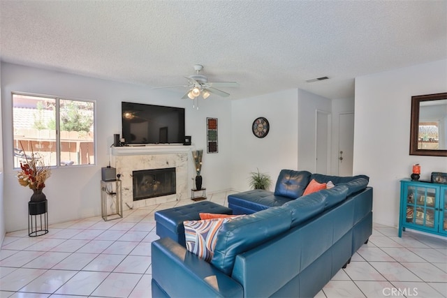 living room with a textured ceiling, a premium fireplace, ceiling fan, and light tile patterned flooring