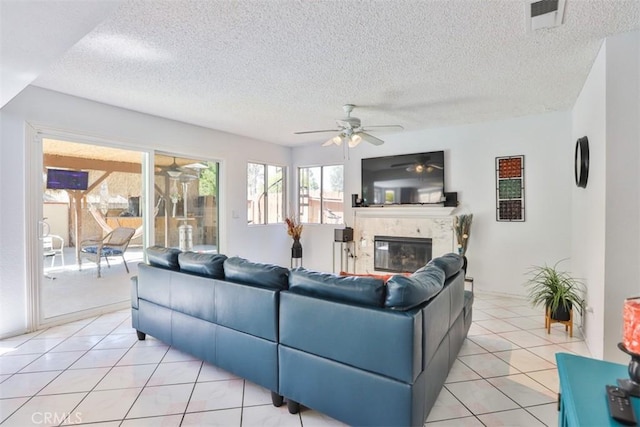 living room featuring ceiling fan, light tile patterned floors, a premium fireplace, and a textured ceiling