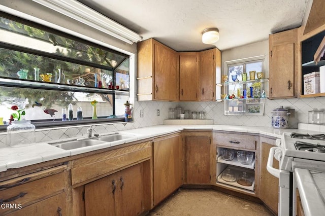 kitchen featuring sink, tile countertops, backsplash, and gas range gas stove