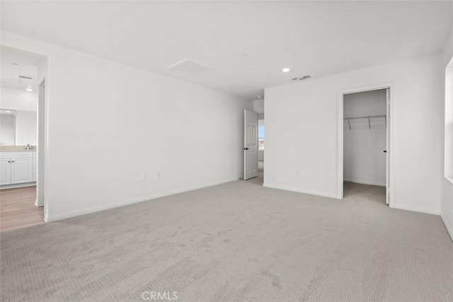 unfurnished bedroom with a walk in closet, light colored carpet, connected bathroom, and a closet