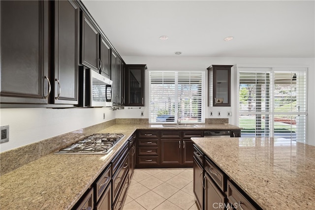 kitchen featuring light stone countertops, dark brown cabinetry, appliances with stainless steel finishes, and light tile patterned floors