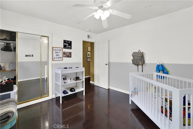 bedroom with ceiling fan, dark hardwood / wood-style floors, a textured ceiling, a nursery area, and a closet