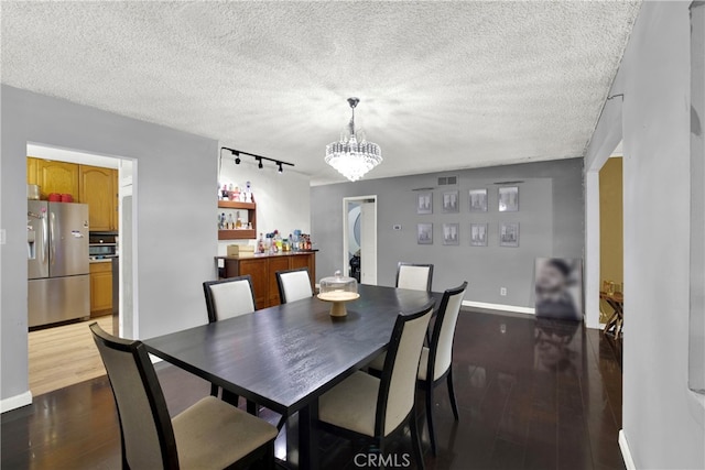 dining space featuring a textured ceiling, an inviting chandelier, dark wood-type flooring, and rail lighting