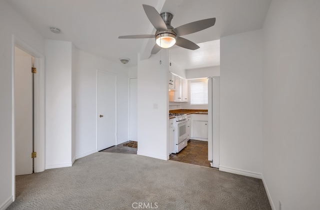 unfurnished bedroom featuring connected bathroom, a ceiling fan, freestanding refrigerator, baseboards, and dark carpet