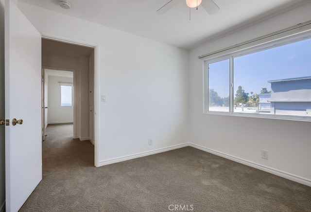 spare room with plenty of natural light, baseboards, dark colored carpet, and a ceiling fan