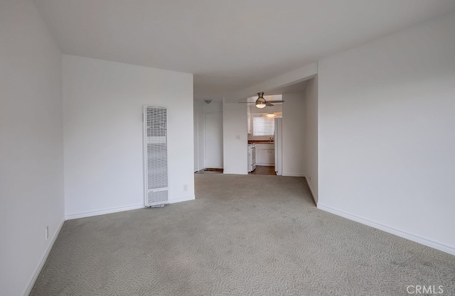 carpeted spare room with baseboards, ceiling fan, and a heating unit