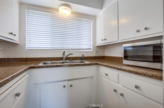 kitchen featuring white dishwasher, sink, and white cabinets