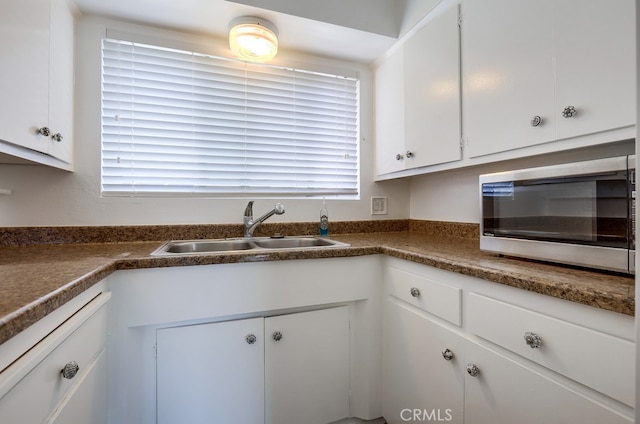 kitchen with stainless steel microwave, a sink, dark countertops, white cabinets, and white dishwasher