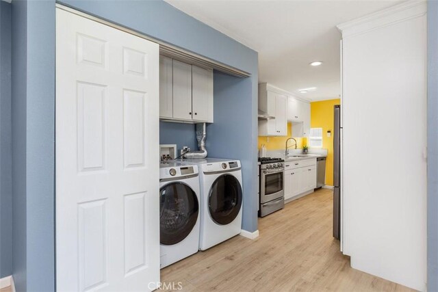 clothes washing area featuring separate washer and dryer, sink, cabinets, and light wood-type flooring