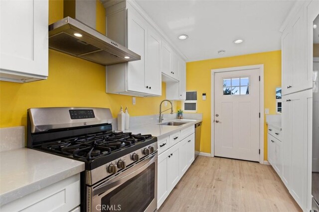 kitchen with sink, wall chimney range hood, appliances with stainless steel finishes, white cabinets, and light wood-type flooring