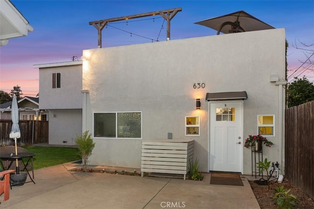 back of property at dusk with a patio, fence, and stucco siding