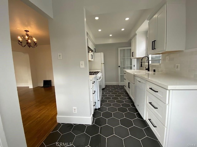 kitchen with light countertops, decorative backsplash, white cabinets, a sink, and white appliances