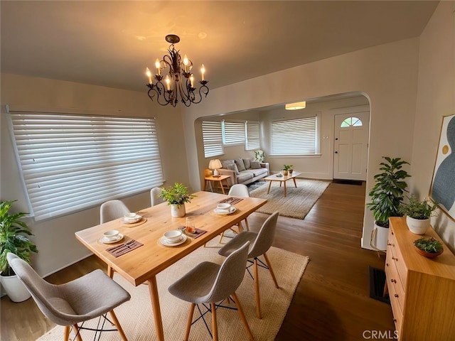 dining space with dark wood-style floors, visible vents, arched walkways, and a chandelier