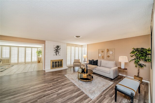 living room featuring a fireplace, wood-type flooring, brick wall, and a textured ceiling