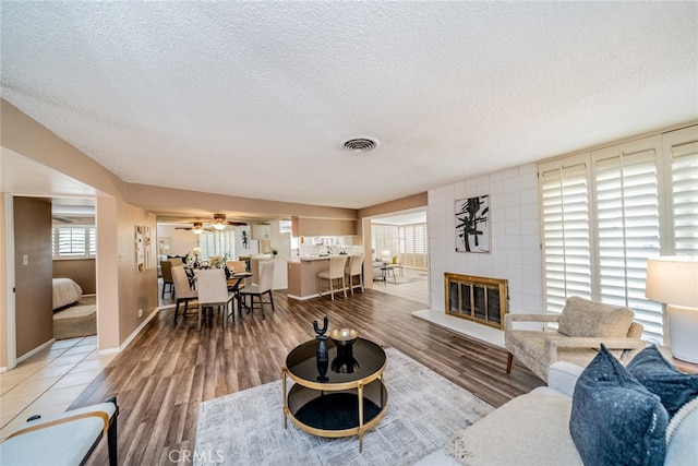 living room featuring hardwood / wood-style flooring, a fireplace, a textured ceiling, brick wall, and ceiling fan