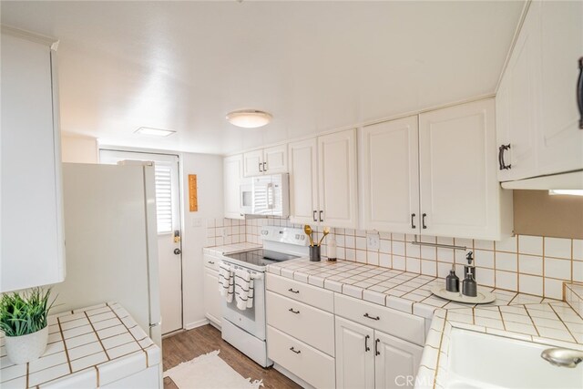 kitchen featuring wood-type flooring, tasteful backsplash, white cabinets, white appliances, and tile countertops