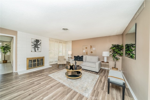 living room featuring a fireplace, light hardwood / wood-style floors, a healthy amount of sunlight, and a textured ceiling