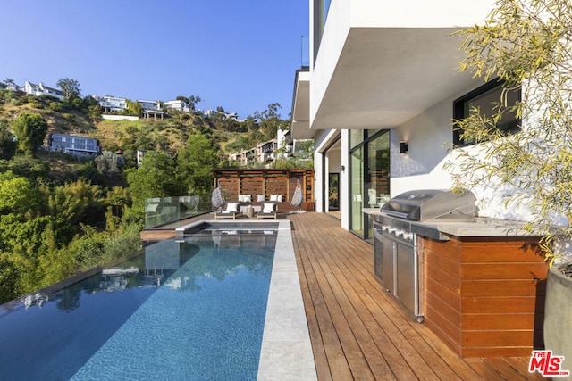 view of swimming pool featuring exterior kitchen, a deck, and grilling area