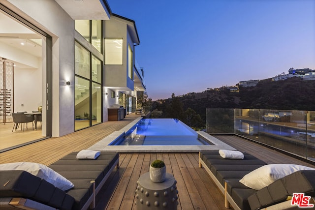 pool at dusk featuring a wooden deck and a jacuzzi