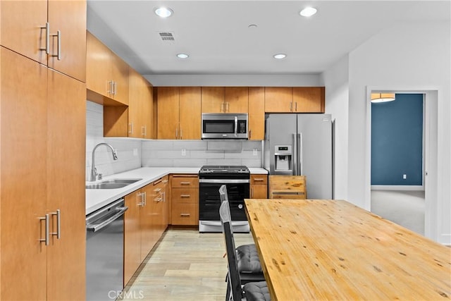 kitchen with tasteful backsplash, stainless steel appliances, sink, and light wood-type flooring