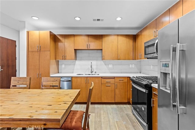 kitchen with tasteful backsplash, appliances with stainless steel finishes, sink, and light hardwood / wood-style flooring