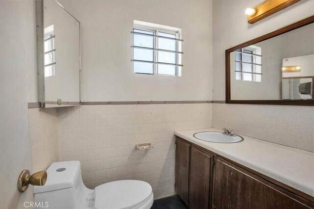 bathroom with tile walls, toilet, a wealth of natural light, and vanity