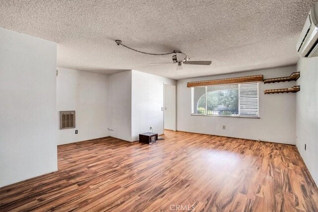 spare room featuring a wall unit AC, a textured ceiling, and hardwood / wood-style floors