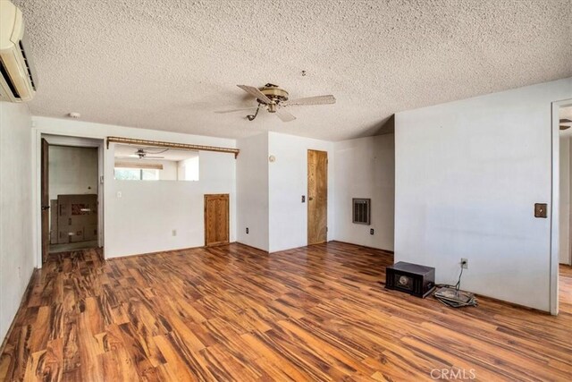 unfurnished living room with an AC wall unit, a textured ceiling, ceiling fan, and hardwood / wood-style flooring