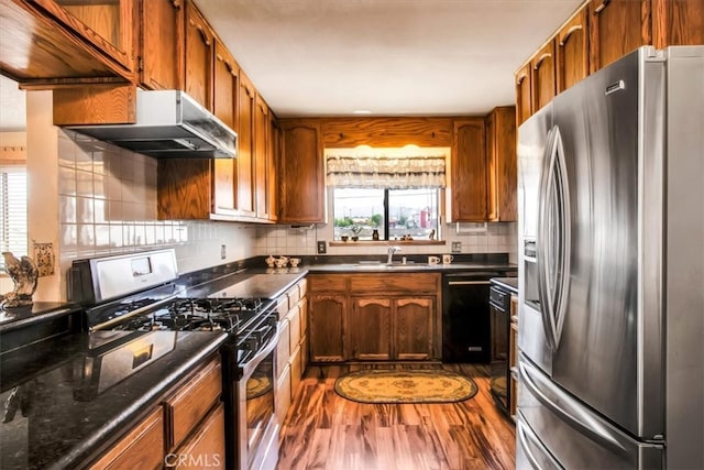 kitchen with dark wood-type flooring, backsplash, range with gas cooktop, black dishwasher, and stainless steel fridge