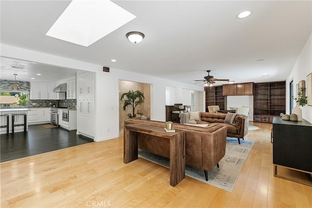 living room with ceiling fan, light hardwood / wood-style flooring, and a skylight