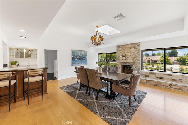 dining space featuring a large fireplace, a chandelier, light hardwood / wood-style flooring, and a healthy amount of sunlight