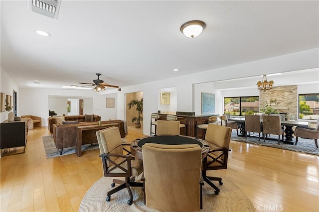 dining room featuring ceiling fan with notable chandelier and light hardwood / wood-style flooring