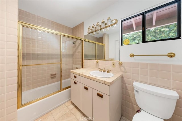 full bathroom featuring combined bath / shower with glass door, vanity, tile walls, tile patterned flooring, and toilet