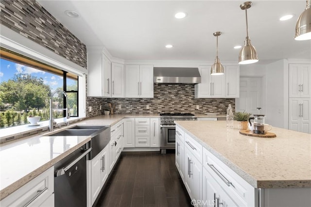 kitchen with wall chimney exhaust hood, stainless steel appliances, white cabinets, a center island, and hanging light fixtures