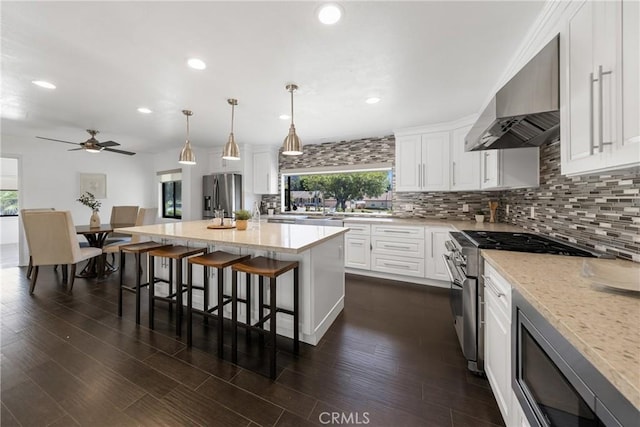 kitchen featuring wall chimney exhaust hood, a center island, a healthy amount of sunlight, and appliances with stainless steel finishes