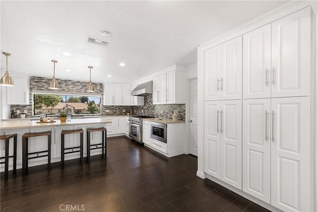 kitchen featuring a breakfast bar, wall chimney range hood, hanging light fixtures, white cabinetry, and stainless steel appliances