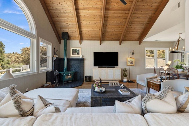 living room with a notable chandelier, a wood stove, beam ceiling, and hardwood / wood-style flooring