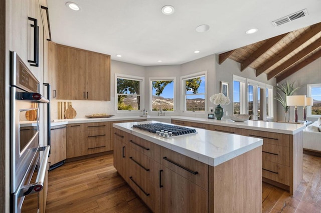 kitchen featuring vaulted ceiling with beams, appliances with stainless steel finishes, hardwood / wood-style flooring, and a kitchen island