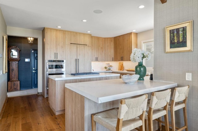 kitchen featuring tile walls, a center island, light hardwood / wood-style flooring, stainless steel appliances, and a kitchen breakfast bar