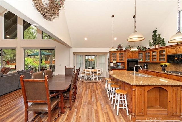 dining space with sink, light hardwood / wood-style floors, and high vaulted ceiling