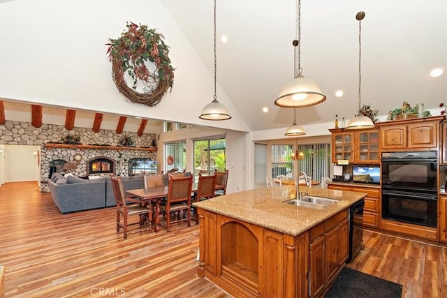 kitchen featuring a fireplace, sink, hanging light fixtures, light stone counters, and black appliances