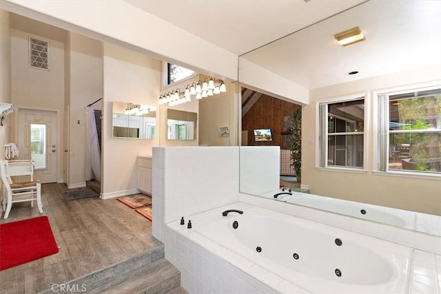 bathroom featuring tiled tub, wood-type flooring, a healthy amount of sunlight, and vanity