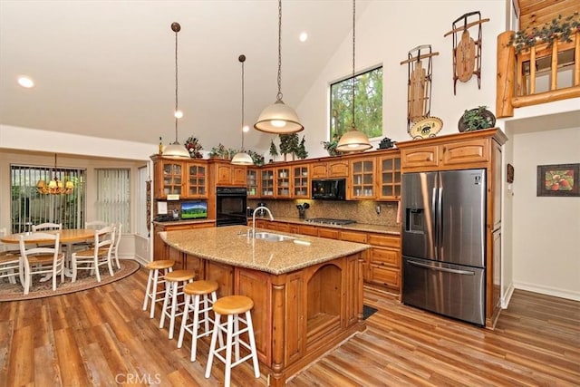 kitchen featuring high vaulted ceiling, hanging light fixtures, a kitchen island with sink, decorative backsplash, and black appliances