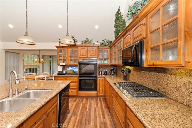 kitchen featuring pendant lighting, sink, light stone counters, black appliances, and light hardwood / wood-style floors